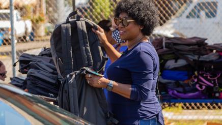 Assemblymember McKinnor reaches for backpacks to give away to passengers in a car