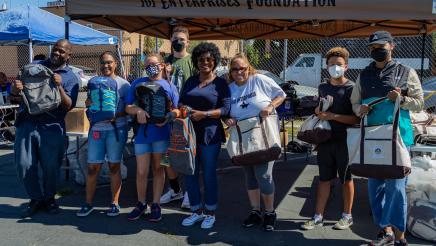 Assemblymember McKinnor and volunteers stand together to pose with backpacks that are ready to be given away
