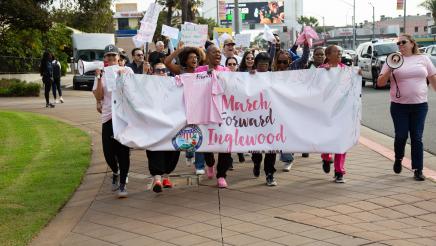 Asm. McKinnor marching down sidewalk with participants, holding up large banner