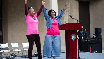 Asm. McKinnor and guest speaker next to podium, holding up arms