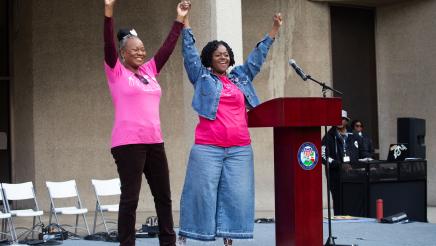 Asm. McKinnor and guest speaker next to podium, holding up arms