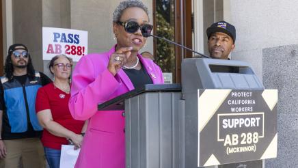 Asm. McKinnor at podium in front of Capitol doors, speaking