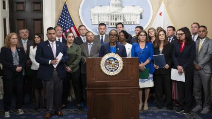Asm. McKinnor at podium, speaking, with fellow legislators standing in support