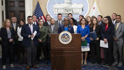 Asm. McKinnor at podium, speaking, with fellow legislators standing in support